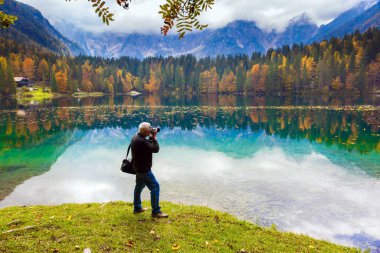 Elinde fotoğraf çantası olan bir adam muhteşem bir manzara. Alpler. Fuzine Gölü. Sarı ağaçlar gölün yeşil, pürüzsüz suyuna yansır. Kuzey İtalya