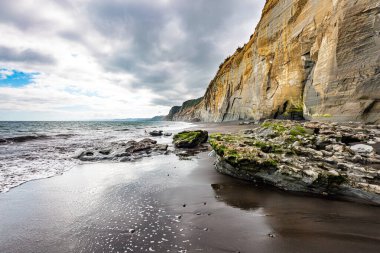 Yumuşak kum üzerindeki ince su tabakası gökyüzünü yansıtır. Pasifik Okyanusu 'nda gelgit var. Yeni Zelanda 'nın muhteşem doğası. Kuzey Taranaki 'nin Pasifik kıyısındaki Saf Beyaz Kayalıklar. 