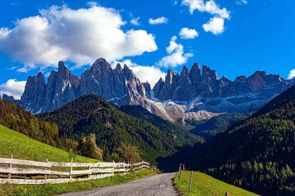 Magnificent Dolomites on a sunny autumn day. Europe, Val de Funes. Tyrol, Italy. Green grassy pastures and mountain roads are fenced with neat wooden fences