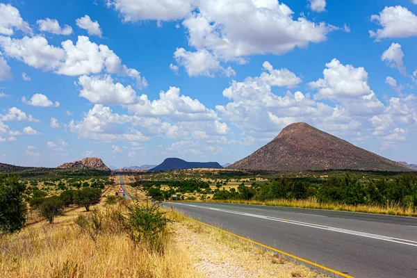 Travel to Africa. The magical desert in Namibia. Hot day, lush clouds float in the blue sky. Paved highway crosses flat savannah