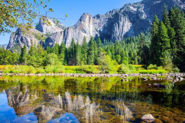 Park Valley 'de güzel bir gün. Resimli El Capitan ve dağ tepeleri Merced Nehri 'nin pürüzsüz sularına yansımaktadır. Yosemite Parkı Sierra Nevada 'nın yamaçlarında yer almaktadır.