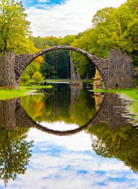 Picturesque narrow bridge in the park Kromlau, Germany. The Devil's Bridge on the Rakots River. The basalt columns of the bridge form a perfect circle with their reflection in the water. 