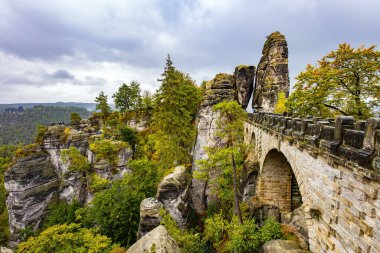The old bridge Bastei is architectural monument protected by the state. The picturesque sandy cliffs of Bastei. Romantic trip to Saxon Switzerland. Germany. Cloudy autumn day. 