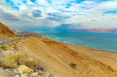 The great wonder of nature is the Dead Sea. The highway runs along the coast of the Dead Sea. Cloudy and clear January day. The sea surface reflects the clouds. Israeli coast