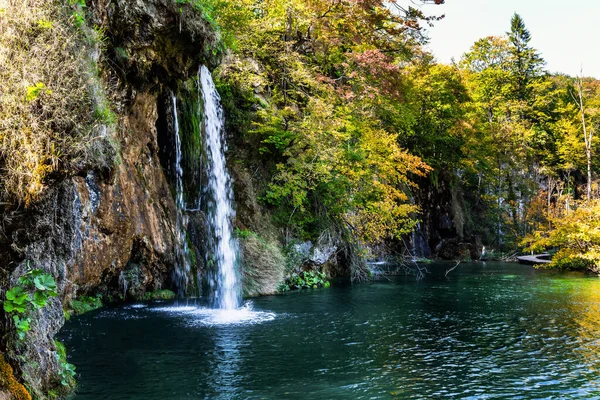 Sunny autumn day. The transparent shallow lake reflects the forest. Plitvice Lakes Park in Croatia, Central Europe. Many picturesque waterfalls flow along the clay cliffs. 