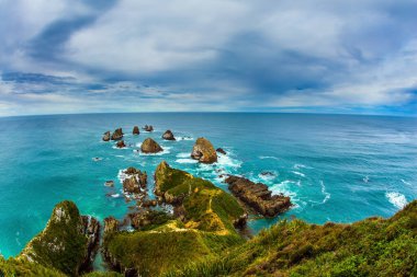 Big stones - rocks along the shore in the ocean surf. New Zealand. The picturesque coast of the Pacific Ocean near Nugget Points. The concept of active, environmental and photo tourism