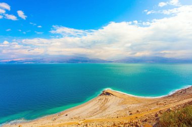 Tuzlu deniz suyunun pürüzsüz yüzeyi gökyüzünü ve bulutları yansıtır. Alçak kış bulutları yeşil deniz suyuna yansıyor. İsrail. Efsanevi Ölü Deniz. 