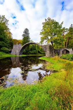 Rakots Nehri 'ndeki Şeytan Köprüsü. Almanya. Köprünün bazalt sütunları sudaki yansımalarıyla mükemmel bir daire oluşturur. Kromlau parkında resim gibi dar bir köprü. 