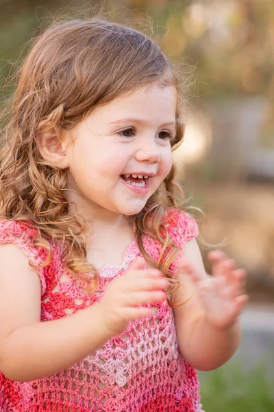 迷人的小女孩卷曲的头发在绿色的草地上玩耍 这个女孩穿着一件粉色针织连衣裙 她笑得很开心 拍了拍手 温暖的春日 — 图库照片