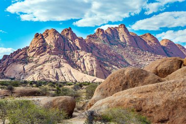 Spitzkoppe, Namibya 'da resim gibi bir kaya yığınıdır. Kaba taneli granitten kırmızı-turuncu Spitzkoppe kalıntıları. Mavi gökyüzünde hafif uçan bulutlar parlıyordu. Afrika. Namibya. 