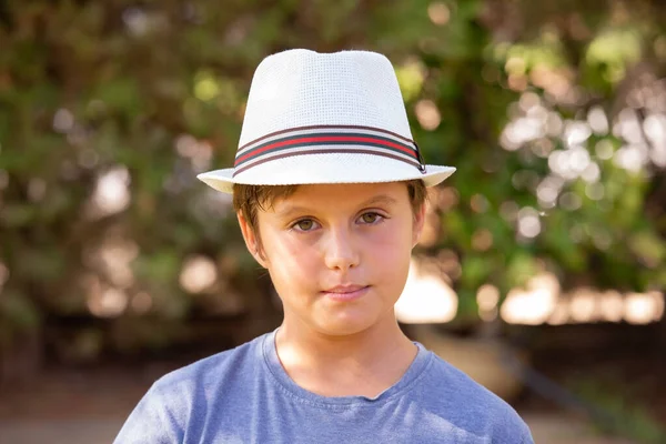 Handsome boy with brown hair and green eyes posing in a white hat. Handsome charming blond boy with blue eyes posing in a white hat. Warm spring day.