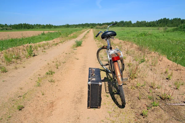 Old valise near old bicycle on rural road — Stock Photo, Image