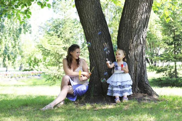 Beautiful mother and daughter blow bubbles in a city park. — Stock Photo, Image