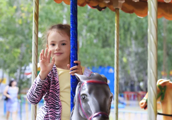 Beautiful little girl spinning on the carousel in the park. — Stock Photo, Image