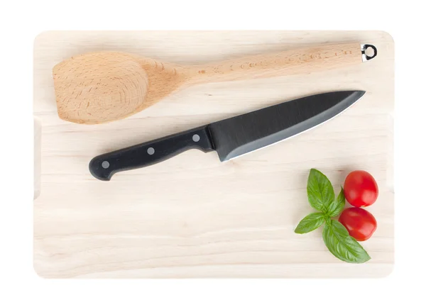 Cooking utensils and tomato with basil over cutting board — Stock Photo, Image