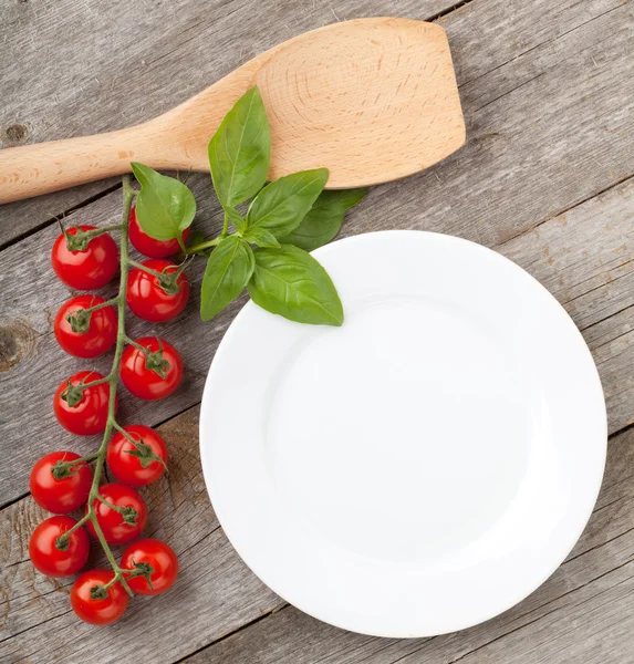 Leerer Teller auf Holz mit Tomaten und Utensilien — Stockfoto