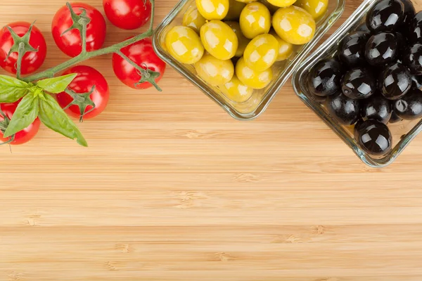 Azeitonas, tomates e manjericão sobre tábua de corte — Fotografia de Stock