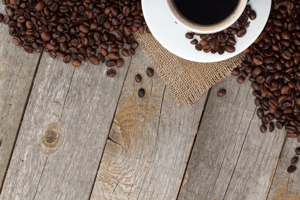 Koffiekopje en bonen op houten tafel — Stockfoto