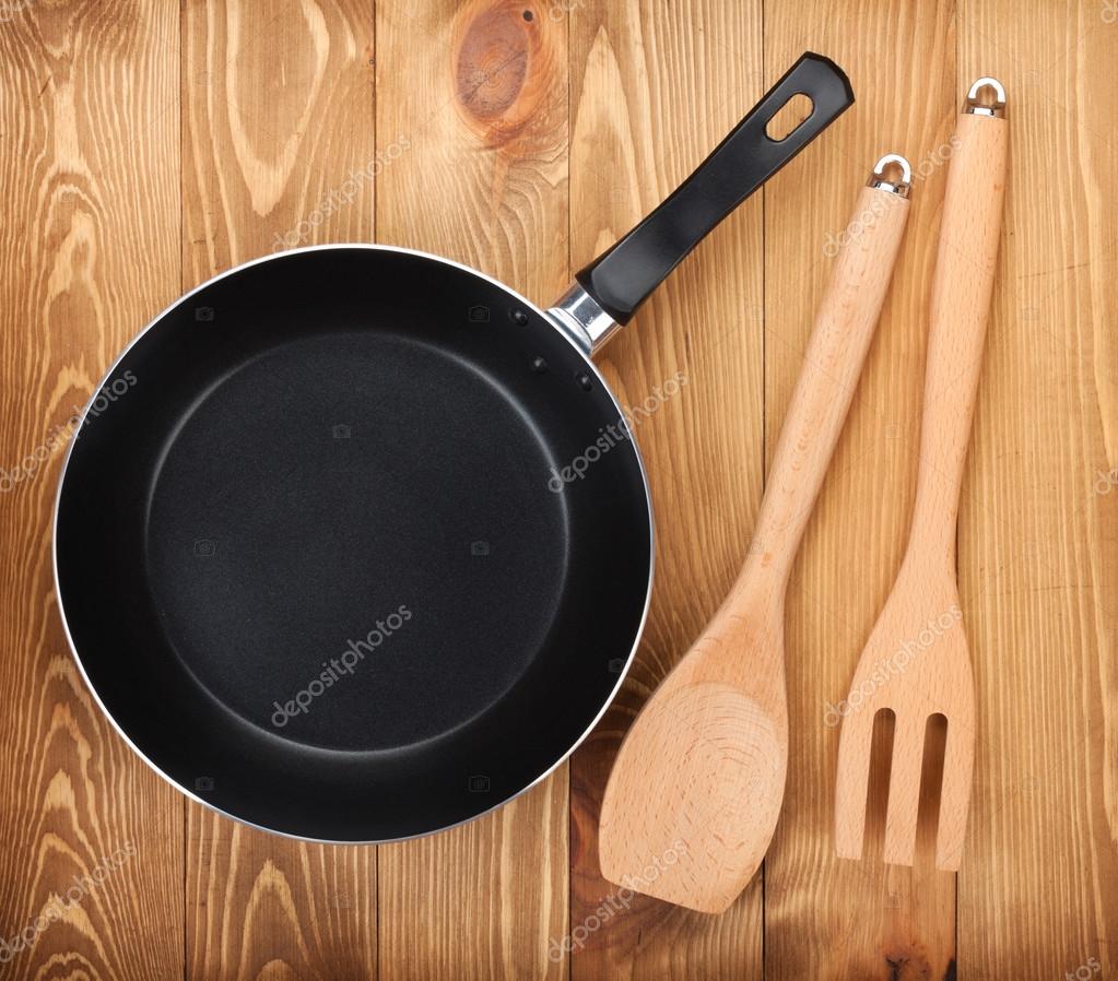 Frying pan and kitchen utensils on wooden table Stock Photo by