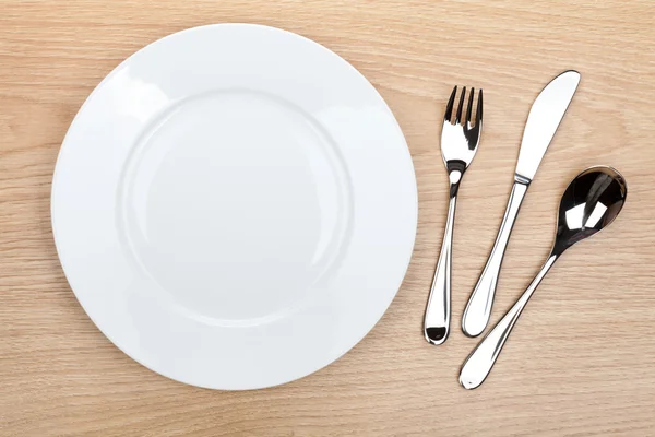 Empty white plate with silverware on wooden table — Stock Photo, Image