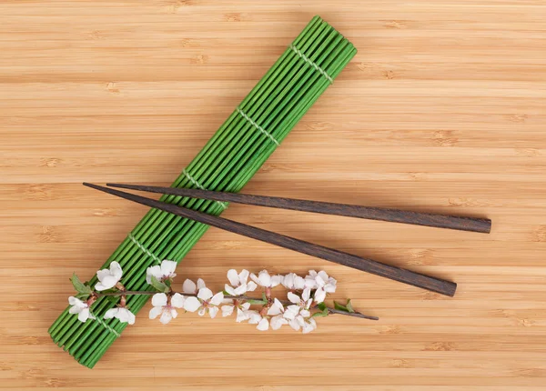 Chopsticks and sakura branch over mat — Stock Photo, Image