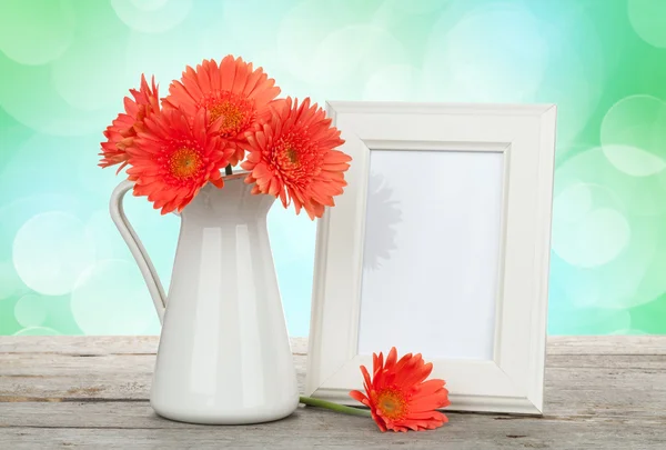 Orange gerbera flowers and photo frame on wooden table — Stock Photo, Image