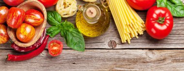 İtalyan yemek malzemeleri. Domates, fesleğen, spagetti makarna, zeytinyağı ve ahşap masada kırmızı biber. Üst görünüm düzlüğü