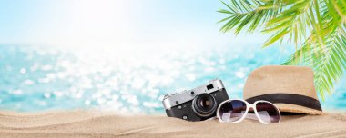 Retro kamera, güneş şapkası ve güneş gözlükleri tropikal plajda palmiye yaprakları ve parlak kumlarla. Yaz tatili ve fotokopi alanı ile seyahat kavramı