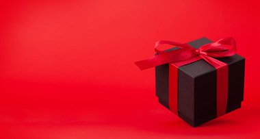 Kırmızı arka planda kırmızı kurdeleli siyah hediye kutusu. Noel, doğum günü ya da sevgililer günü için yer var mı?