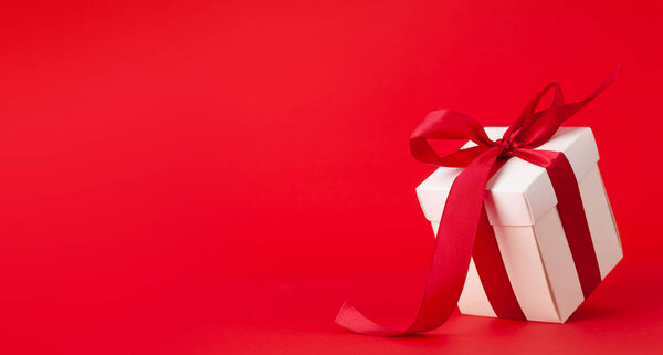 White gift box with red ribbon over red background. With space for your Christmas, birthday or Valentines day greetings