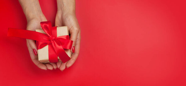 Woman hands holding Christmas or Valentine's Day gift box on red background. Top view flat lay with copy space