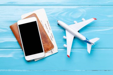 Seyahat ve tatil konsepti. Aksesuarlar ve eşyalar. Pasaport, bilet ve uçak oyuncağı yerine akıllı telefon. Üst görünüm düzlüğü kopyalama alanı ile yatıyordu