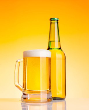 Bira şişesi ve bira, sarı arka planda bira. Stüdyo çekimi