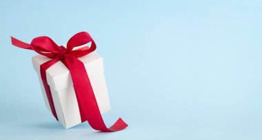 Mavi arka planda kırmızı kurdeleli beyaz hediye kutusu. Noel, doğum günü ya da sevgililer günü için yer var mı?