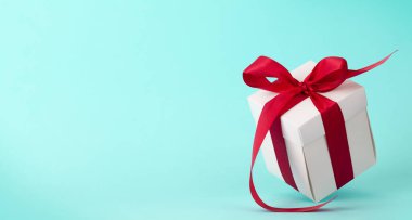 Mavi arka planda kırmızı kurdeleli beyaz hediye kutusu. Noel, doğum günü ya da sevgililer günü için yer var mı?