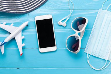 Seyahat ve tatil konsepti. Aksesuarlar ve eşyalar. Güneş şapkası, güneş gözlüğü, akıllı telefon ve yüz maskesi. Üst görünüm düzlüğü kopyalama alanı ile yatıyordu