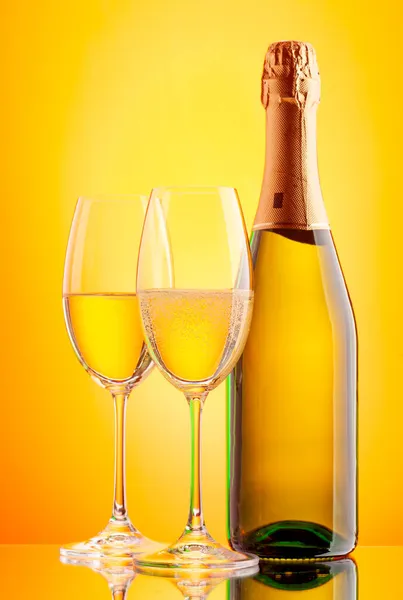 两杯香槟和一个闪闪发光的酒瓶黄底以上 — 图库照片