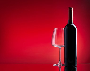 Kırmızı şarap kadehi ve kırmızı zemin üzerinde fotokopi alanı olan şişe.