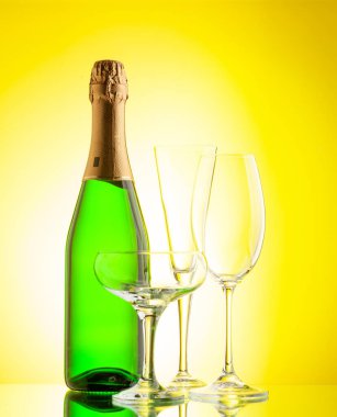 Şampanya bardakları ve köpüklü şarap şişesi. Sarı arkaplan