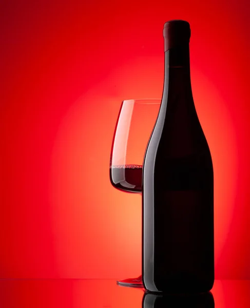 赤ワイングラスとコピースペース付きの赤の背景にボトル — ストック写真