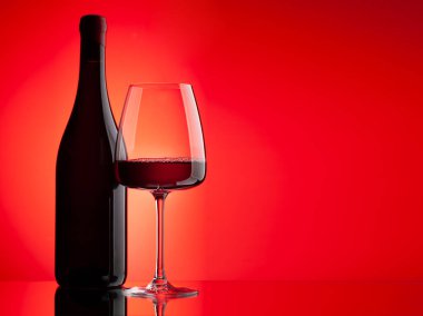 Kırmızı şarap kadehi ve kırmızı zemin üzerinde fotokopi alanı olan şişe.