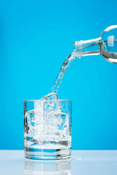 Frischwasser Aus Flasche Glas Mit Eiswürfeln Vor Blauem Hintergrund — Stockfoto