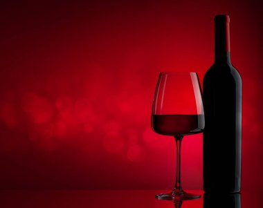 Kırmızı şarap kadehi ve kırmızı zemin üzerinde fotokopi alanı olan şişe.