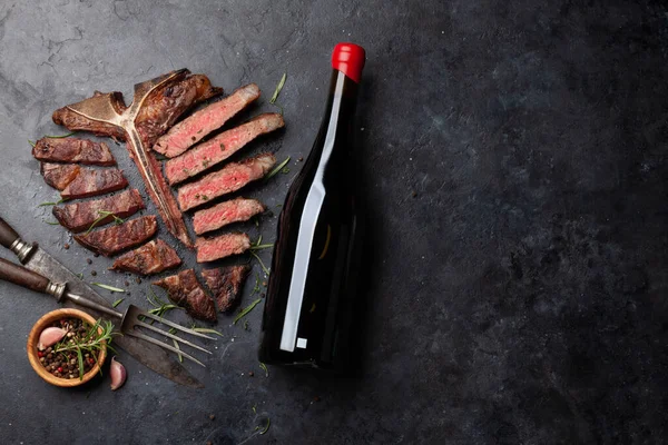 Grilled porterhouse beef steak and wine bottle. Sliced T-bone with herbs and spices. Top view flat lay with copy space