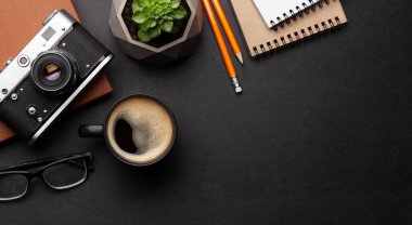 Ofis masasında malzemeler, fotoğraf makinesi ve siyah deri masanın üzerinde kahve. Üst görünüm düzlüğü kopyalama alanı ile yatıyordu