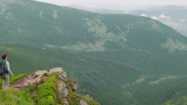Жінка з рюкзаком стоїть на скелі в горах — стокове відео