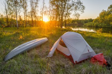 Gün doğumunda kamp çadırı ve kanoyla nehir manzarası