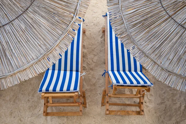 Boş sahilde saman plaj şemsiyeleri ve iki güneş yatağı. — Stok fotoğraf