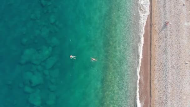 Tiro aéreo de casal flutuando em uma água do mar tranquila em uma praia vazia — Vídeo de Stock