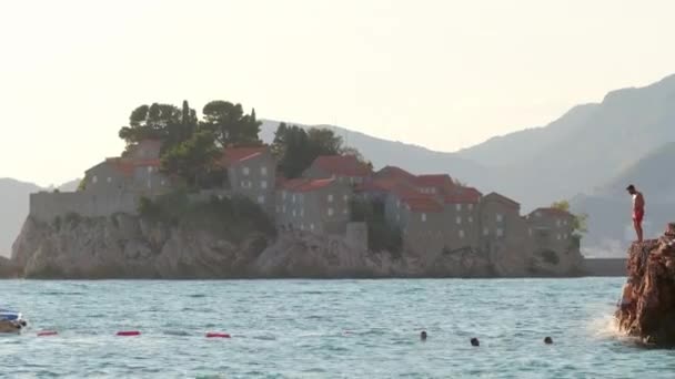 Karadağ 'ın arka planında Sveti Stefan adasıyla denize atlayan Cliff. — Stok video